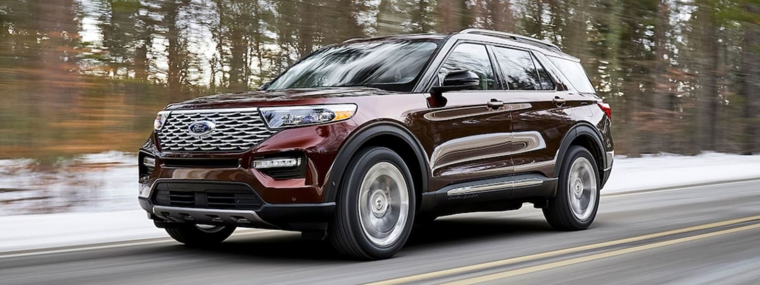 a red ford explorer driving down a road in front of trees and a snow covered forest in the background