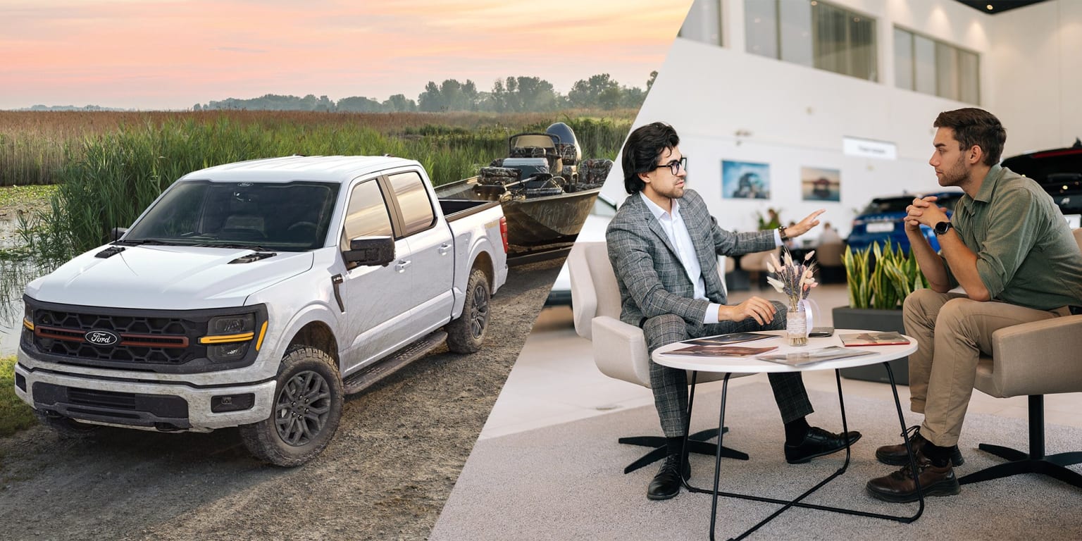 A white pickup truck with outdoor gear on its roof stands in a grassy field, while two people converse at a small table in the foreground.