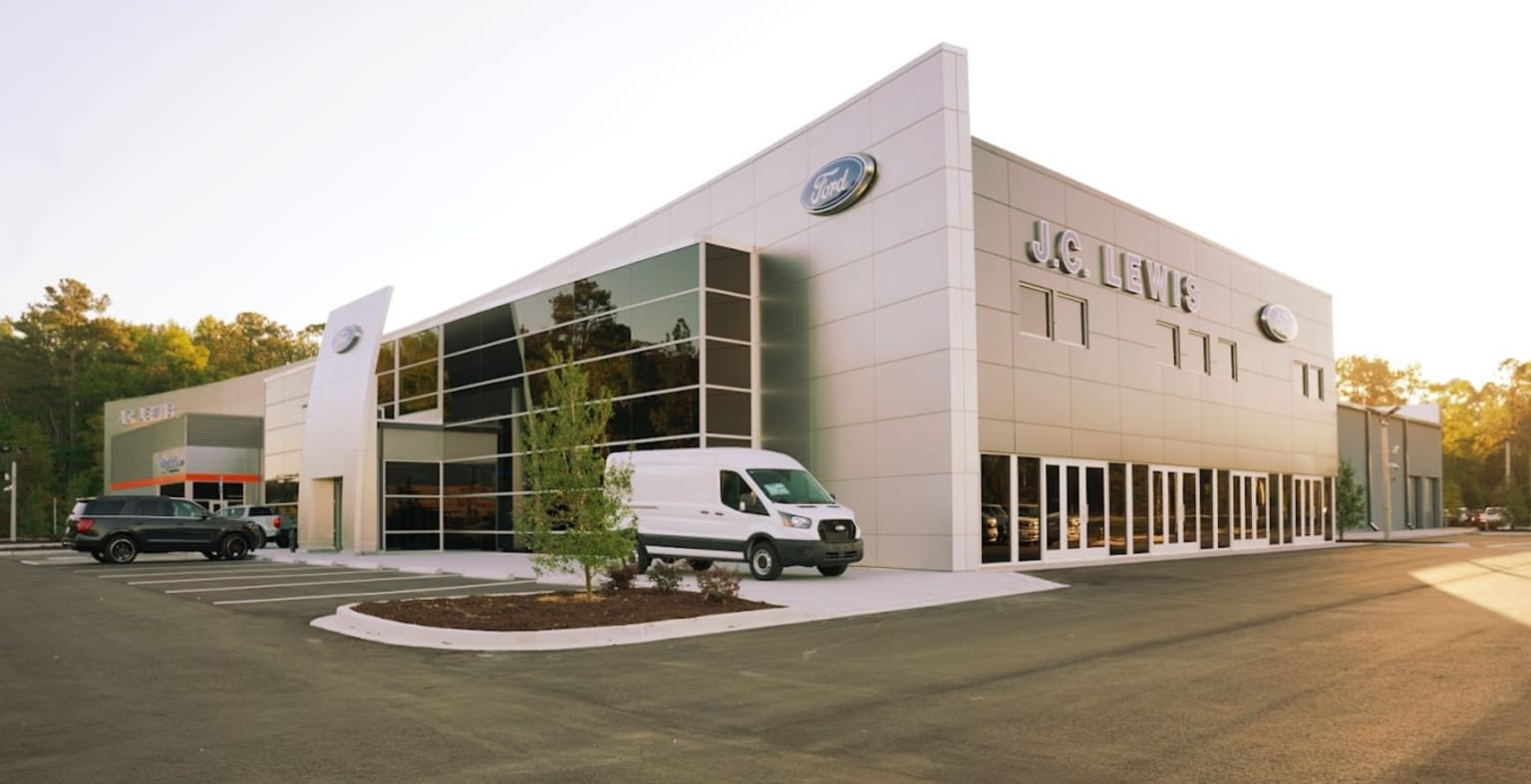 a white van is parked in front of a building with cars parked in front of it and a truck parked in front of it