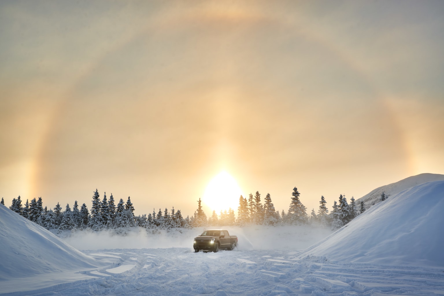 a car driving down a snow covered road with a rainbow in the sky above it and trees in the background