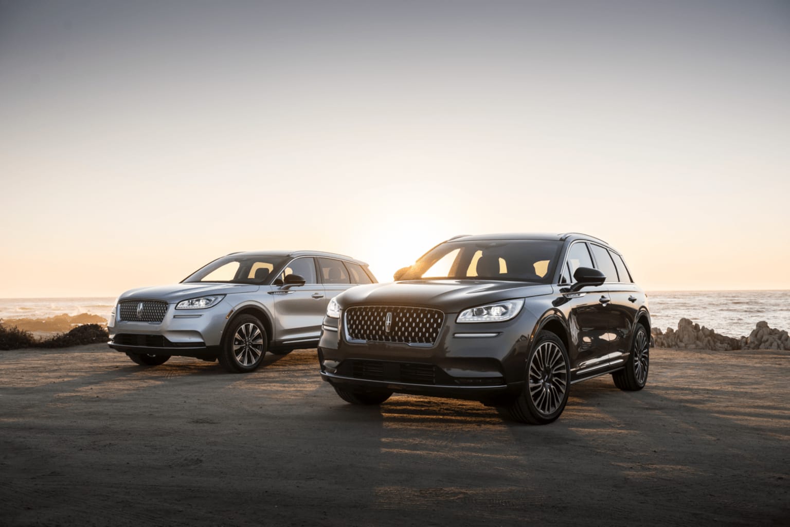 Luxury SUVs parked on a road with a scenic sunset sky in the background.