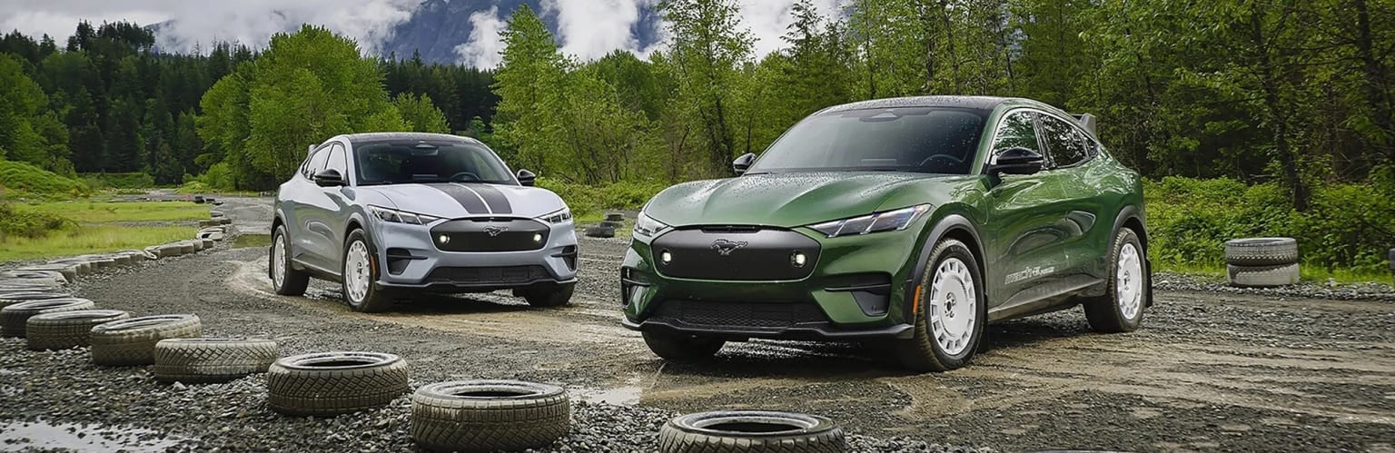 Two green SUVs parked on a dirt road surrounded by a lush, forested landscape.