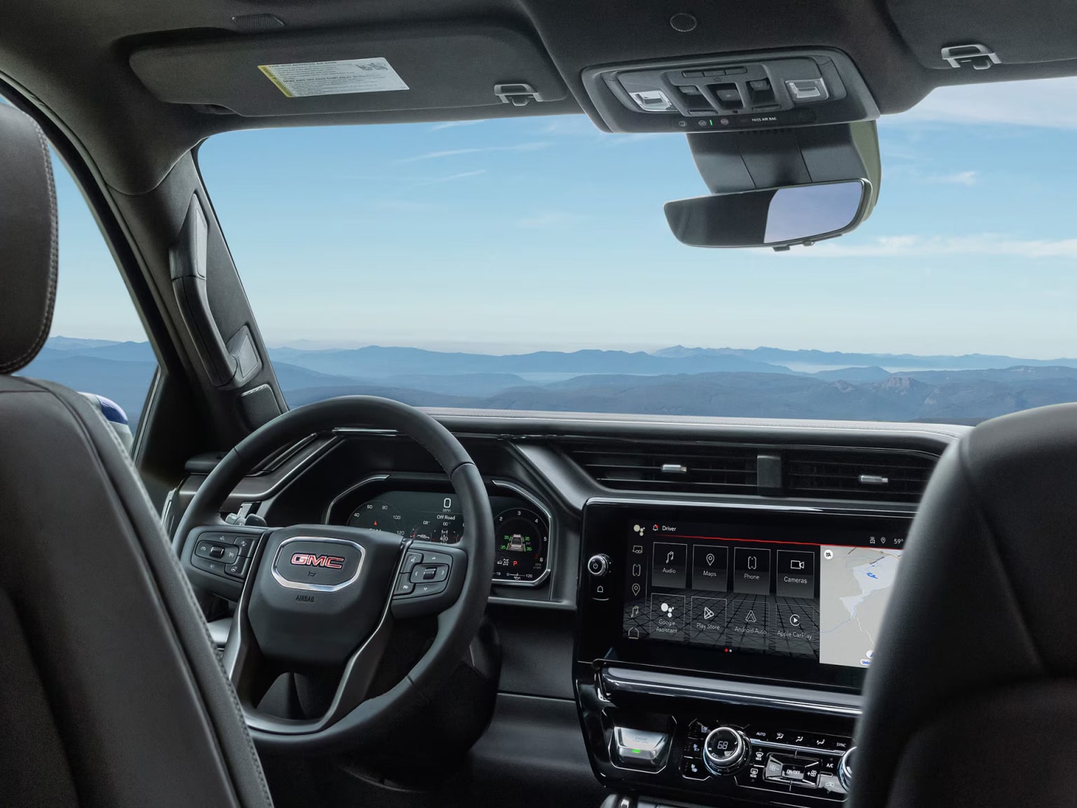The image shows the interior of a vehicle with a steering wheel, dashboard, and controls, with a scenic mountain landscape visible through the windshield in the background.