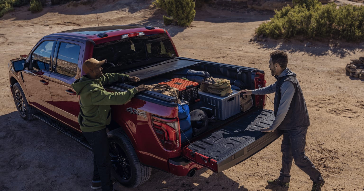 A red pickup truck being loaded with various items in a rugged, sandy landscape with trees in the background.