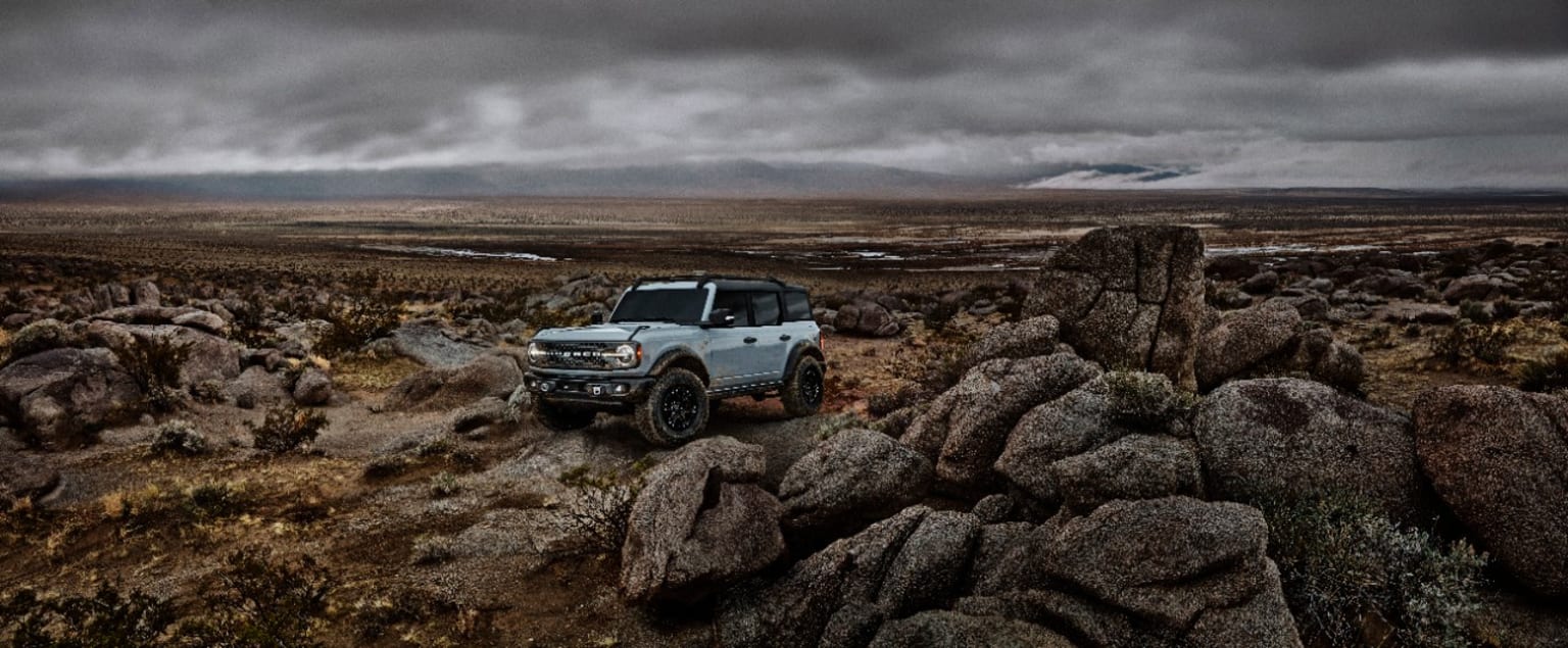 a truck is parked on the side of a rocky hill in the middle of a field under a cloudy sky