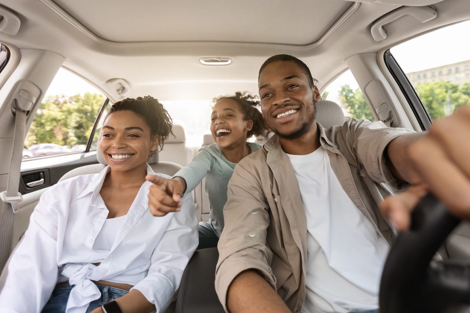 a group of people sitting in the back of a car with a steering wheel and a woman pointing at the camera