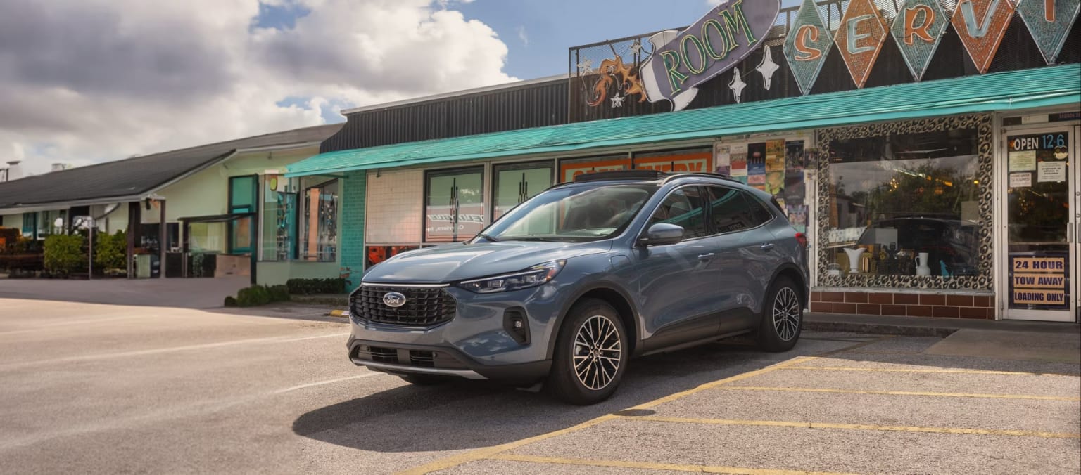 A silver SUV is parked in the foreground, with a colorful storefront and cloudy sky visible in the background.