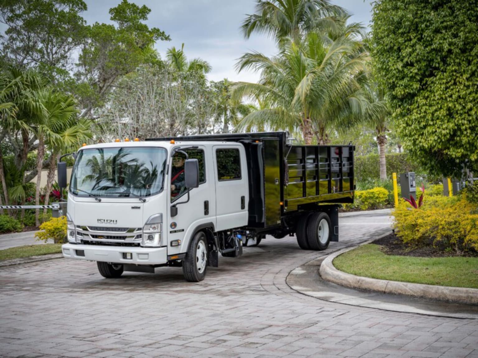 A white dump truck parked on a driveway with palm trees and shrubbery.