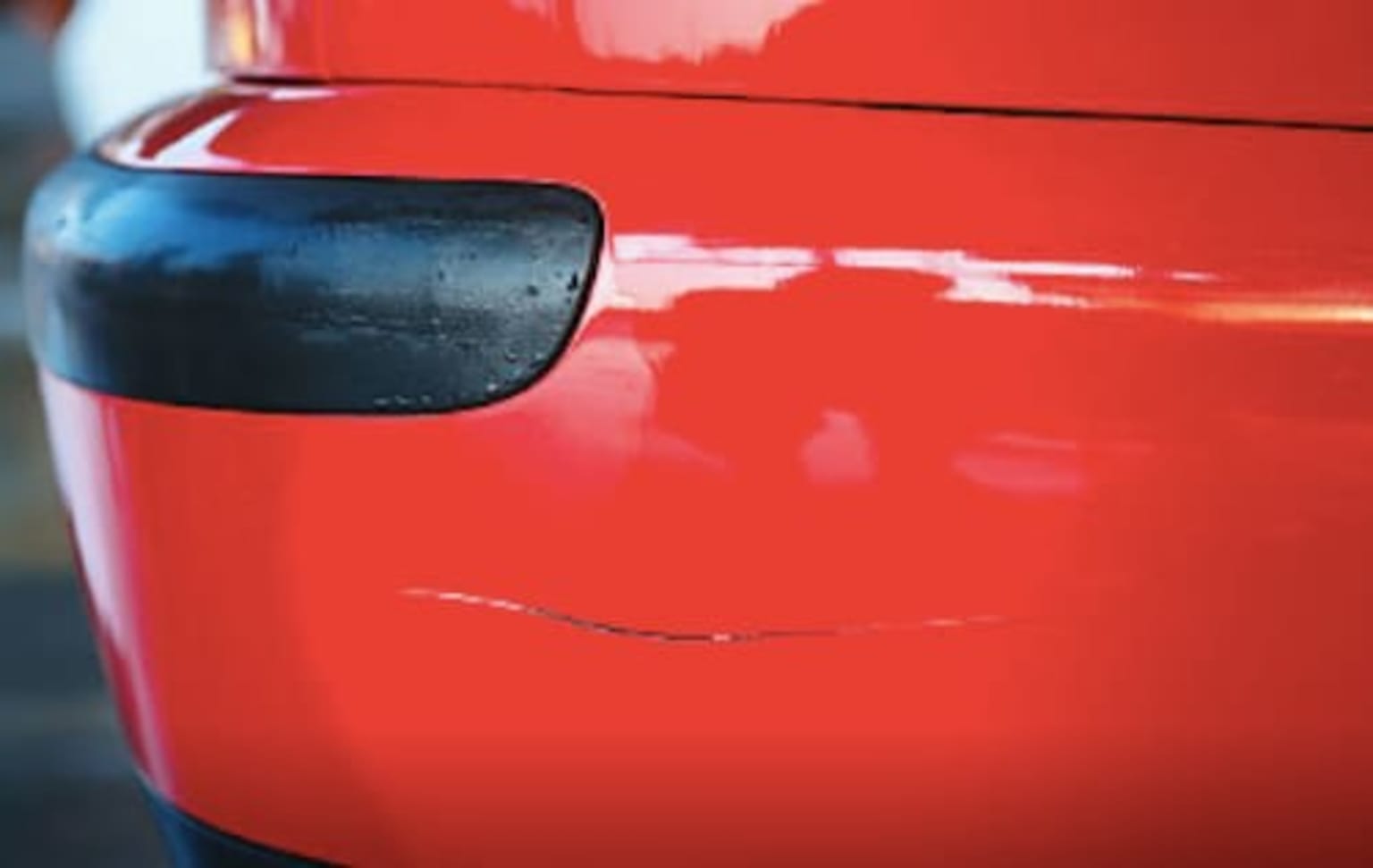 a close up of the side of a red car with a black strip on the side of the car