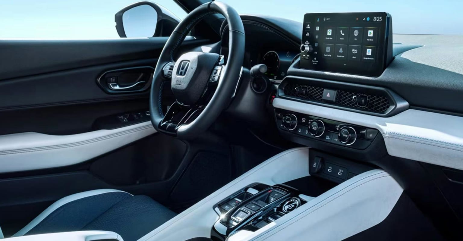 A modern car interior with a sleek dashboard and infotainment screen in the foreground, and a bright sky visible through the windows in the background.