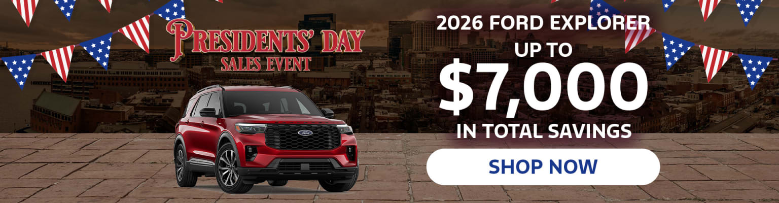 A red SUV is prominently displayed in the foreground, with a promotional banner for a Presidents' Day sales event and a 2026 model advertisement in the background.