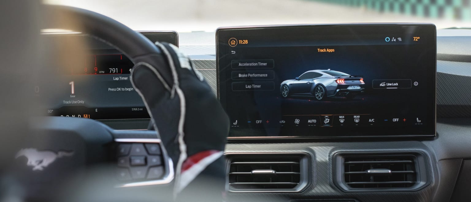 The image shows the interior of a vehicle, with a large display screen in the center console displaying information about a vehicle, in the background.