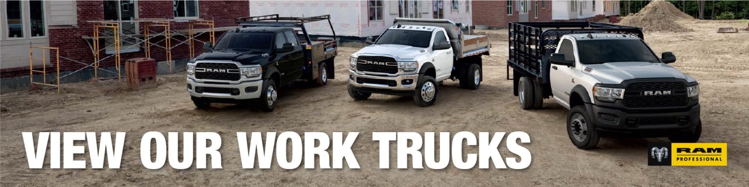 Three work trucks are parked on a dirt lot in front of a building under construction.