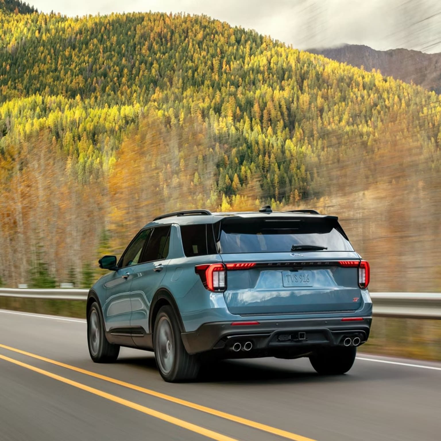 SUV driving on a winding mountain road through a vibrant autumn forest landscape.