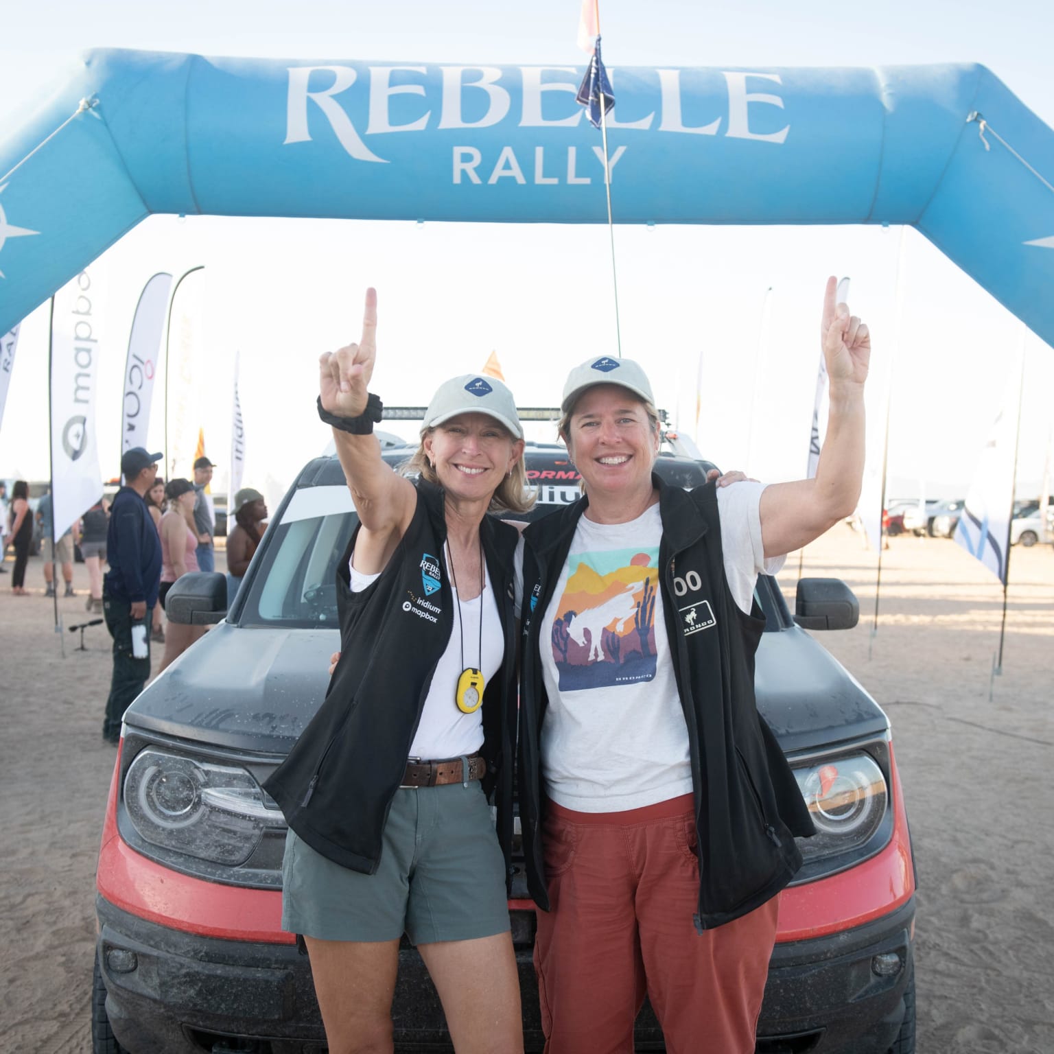 a couple of women standing in front of a truck under a blue sign that says rebbele rally