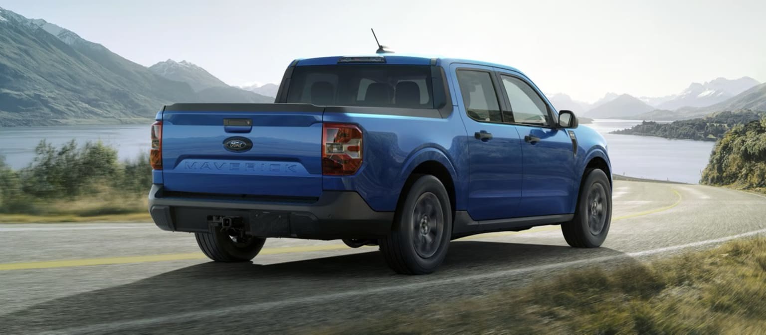 A blue pickup truck in a scenic mountainous landscape with a body of water in the background.