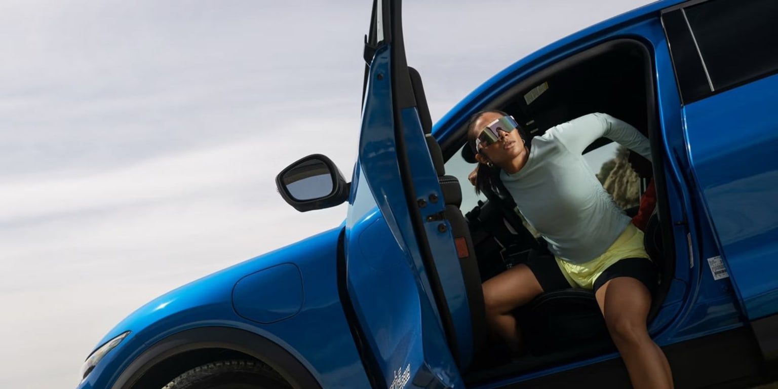 A person sitting in the driver's seat of a blue car with the door open, the sky visible in the background.