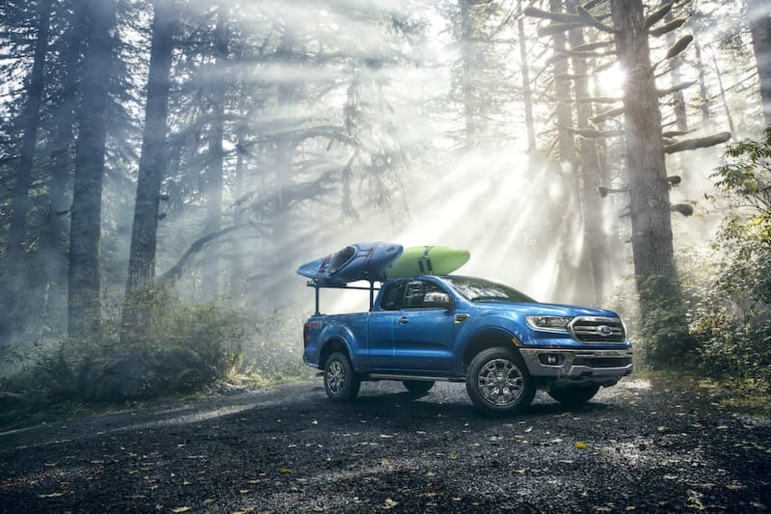 a blue pick up truck with a kayak on top of it's roof parked in the middle of a forest