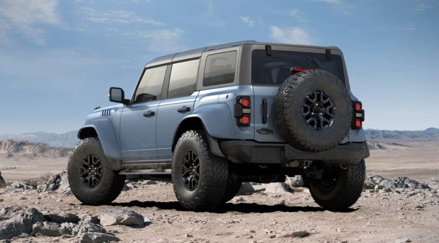 An off-road vehicle with large tires on a rocky, desert-like terrain against a backdrop of a cloudy sky.