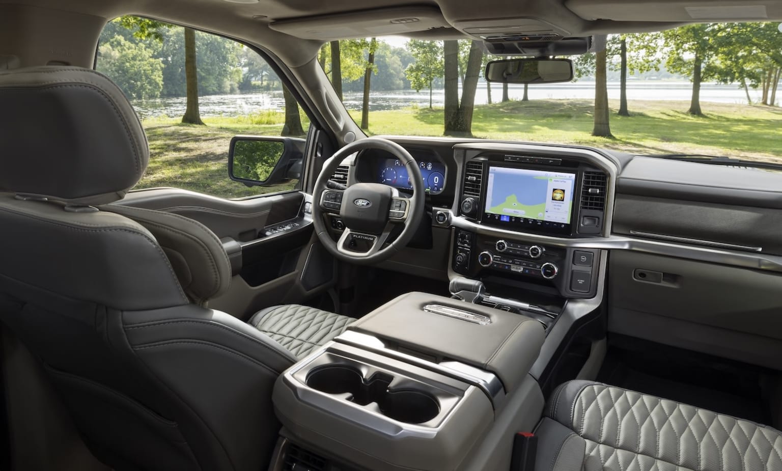 Interior view of a vehicle with dashboard, steering wheel, and seats. Background features a park-like setting with trees and greenery.