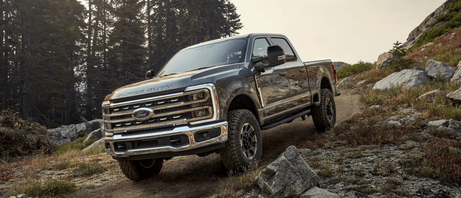 An off-road pickup truck maneuvers through rocky, forested terrain, displaying its impressive capabilities.