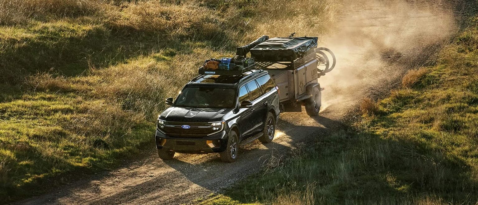 A black SUV towing a camping trailer driving through a grassy field.