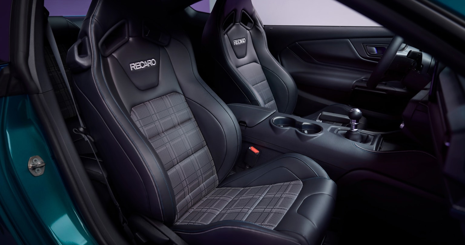 The image displays a black leather sports seat in the foreground and a dark, minimalist dashboard in the background within a car's interior.