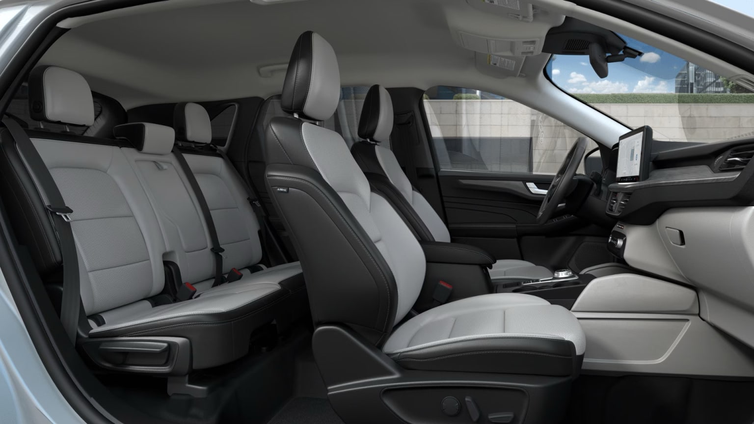 The image shows the interior of a vehicle with multiple seats and a steering wheel visible. The seats are upholstered in a combination of black and light-colored materials, set against a bright, outdoor background.