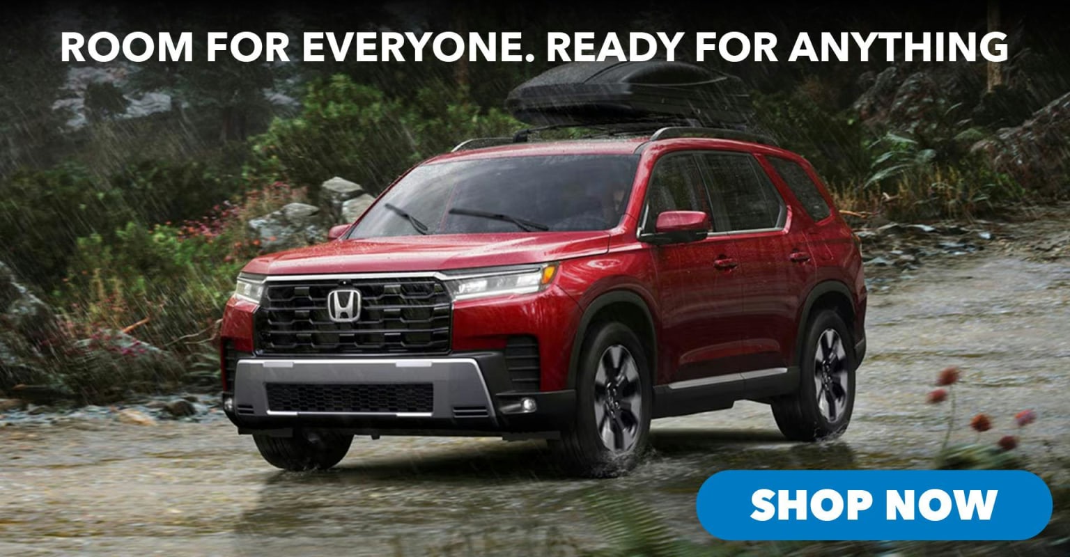 SUV with a roof rack parked on a wet, rocky path with lush green foliage in the background.