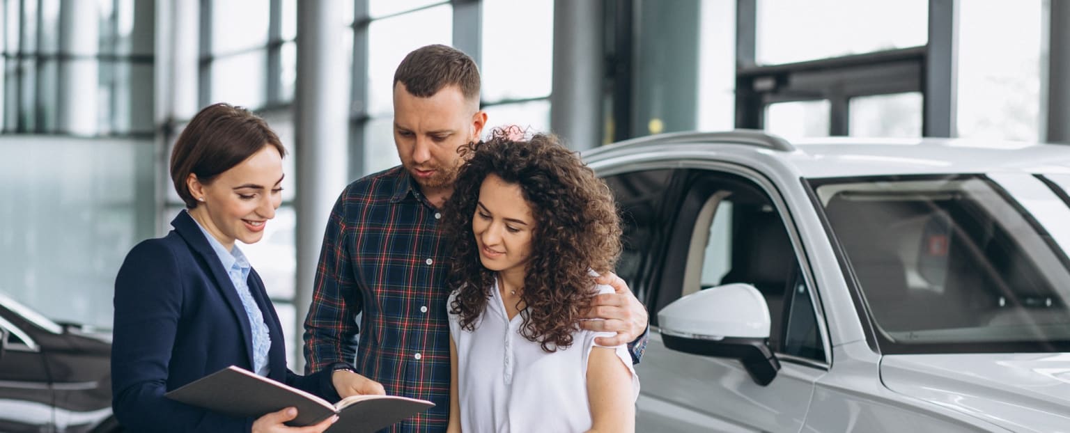 a man and a woman looking at a book in a car showroom next to a silver car and a man in a suit