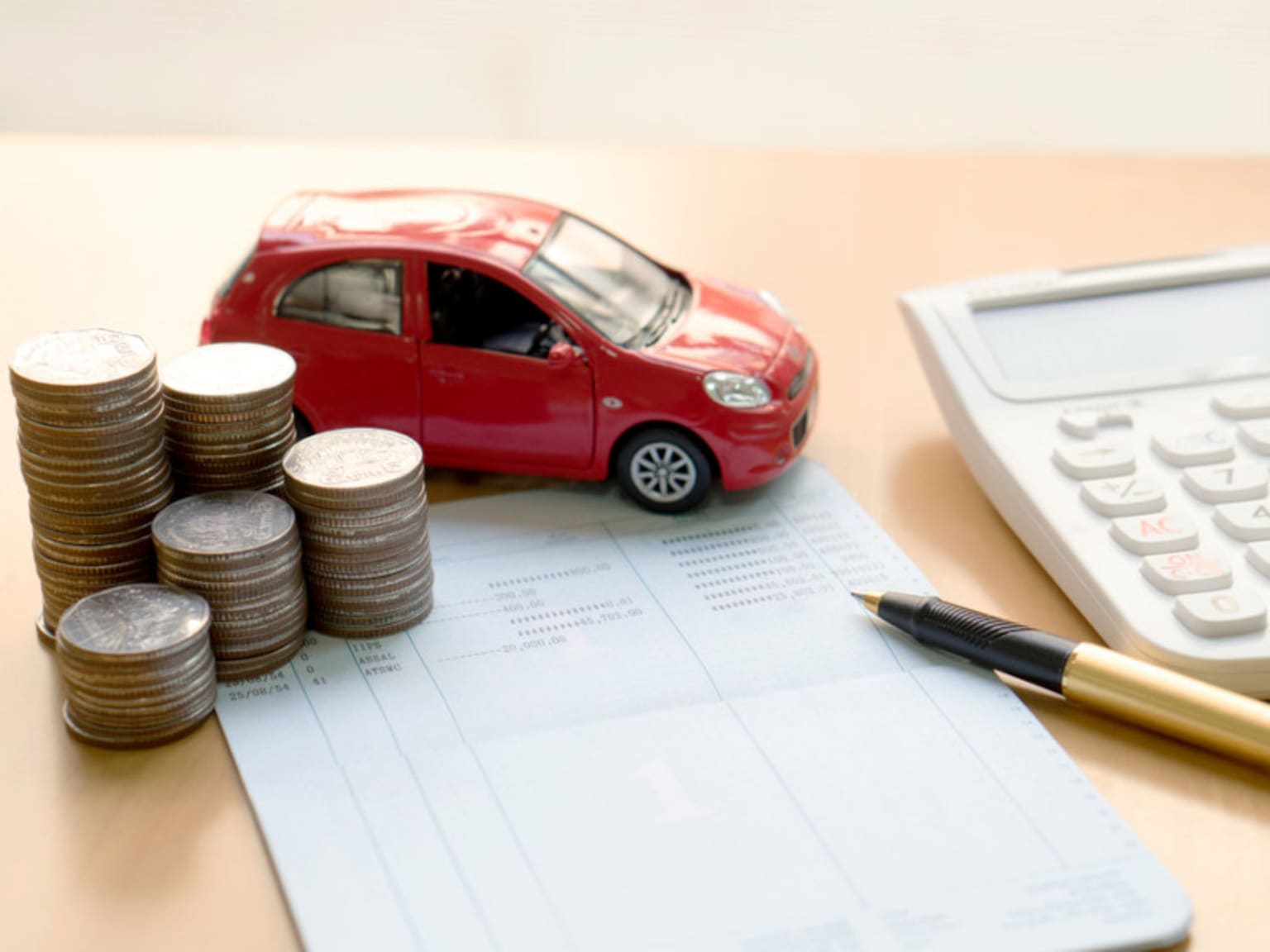 A red toy car, stacks of coins, a calculator, and a pen are arranged on a document, suggesting financial planning or budgeting for a vehicle purchase.