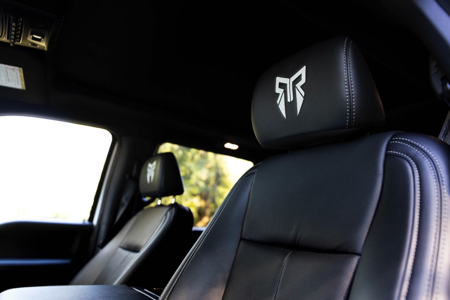 The image shows the interior of a vehicle, with a black leather seat featuring a distinctive logo on the headrest.