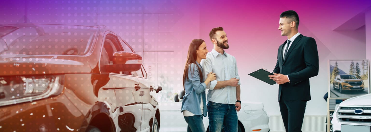A couple talking to a salesperson in front of a car at a dealership.