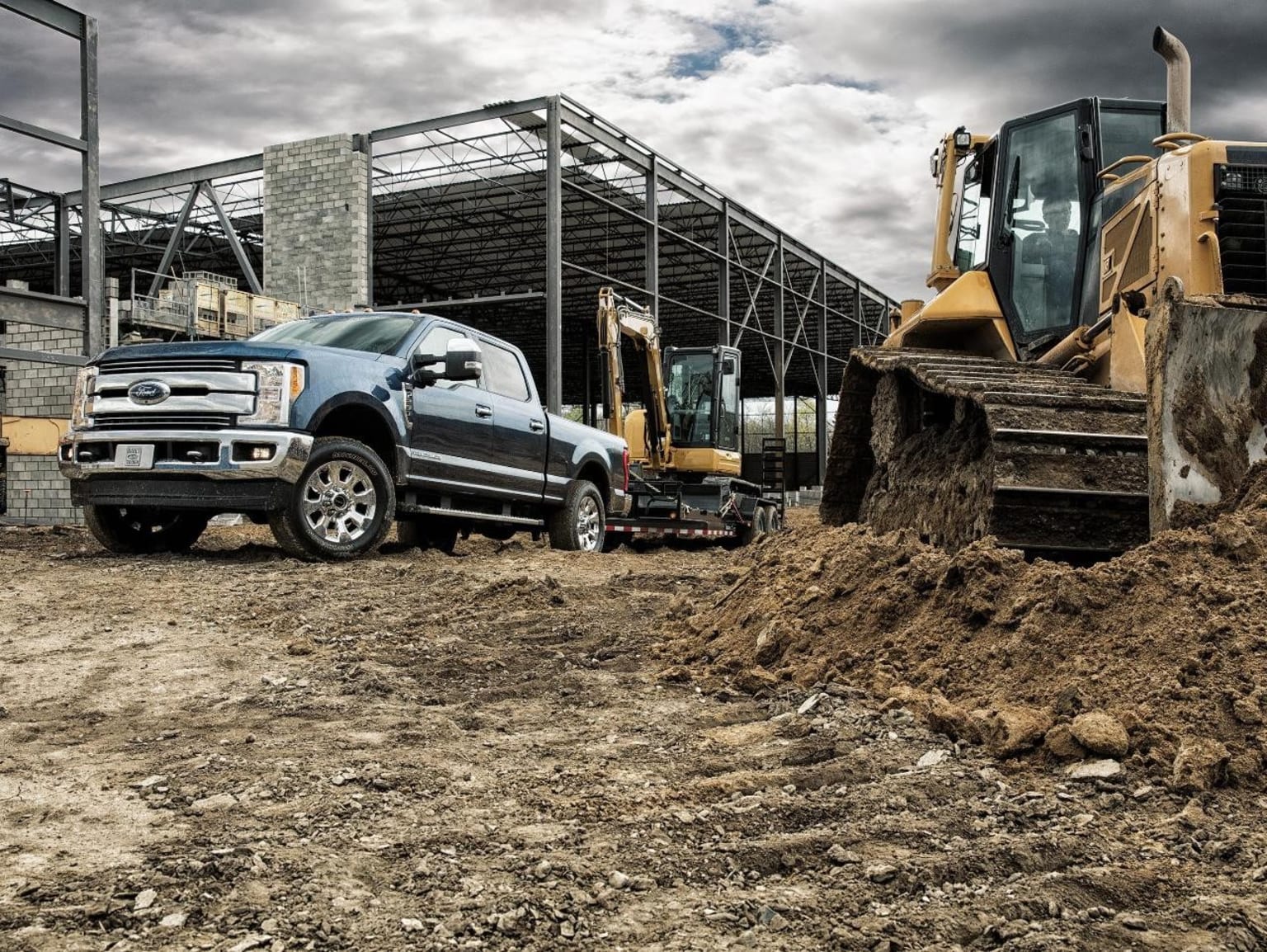 Construction site scene with heavy-duty truck and bulldozer in foreground and partially constructed steel-framed building in background.