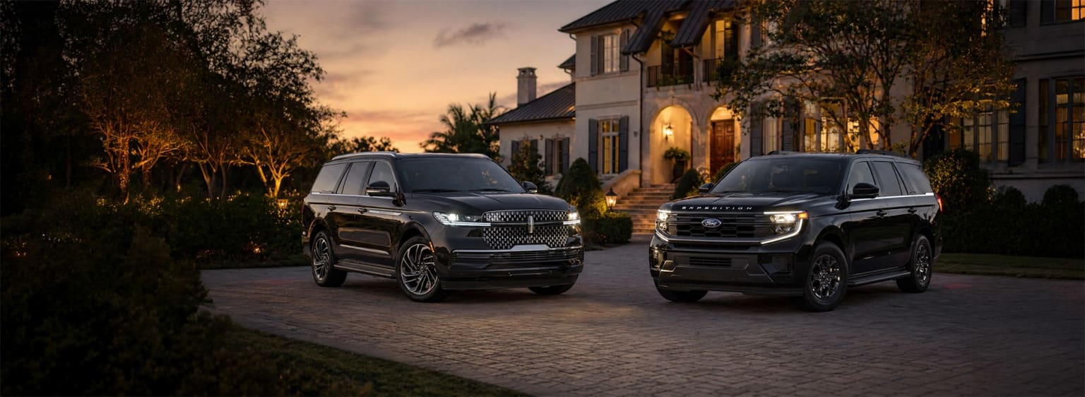 Luxurious SUVs parked in driveway of elegant house with picturesque sunset in background.