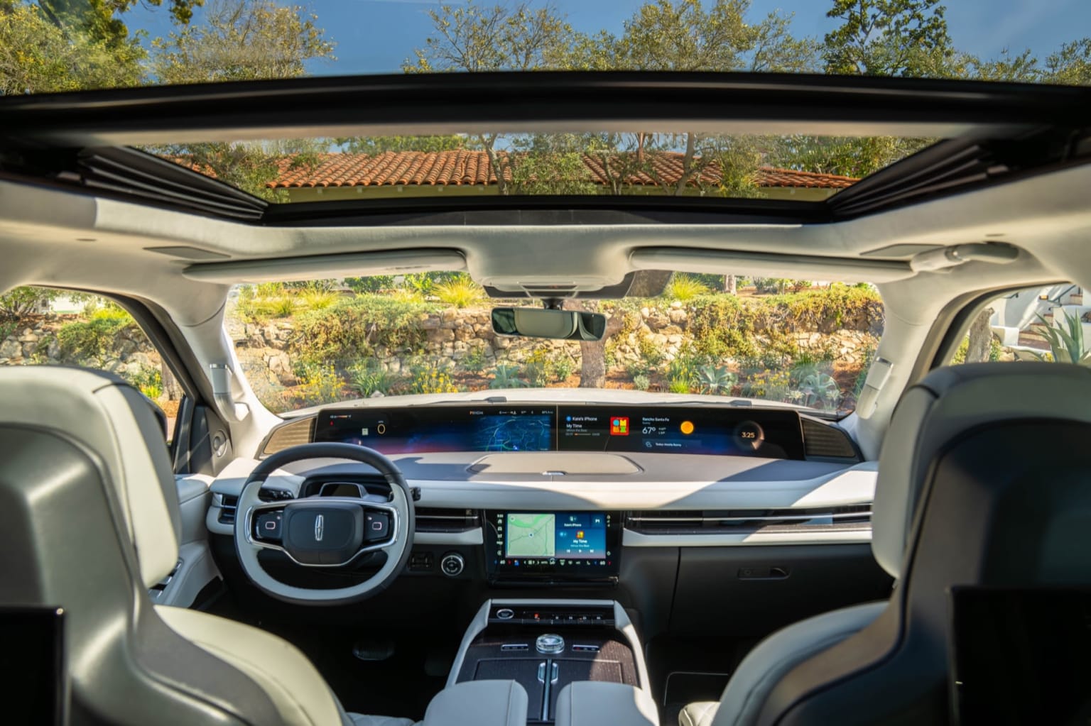 Interior of a modern vehicle with a panoramic sunroof showcasing a lush landscape outside.