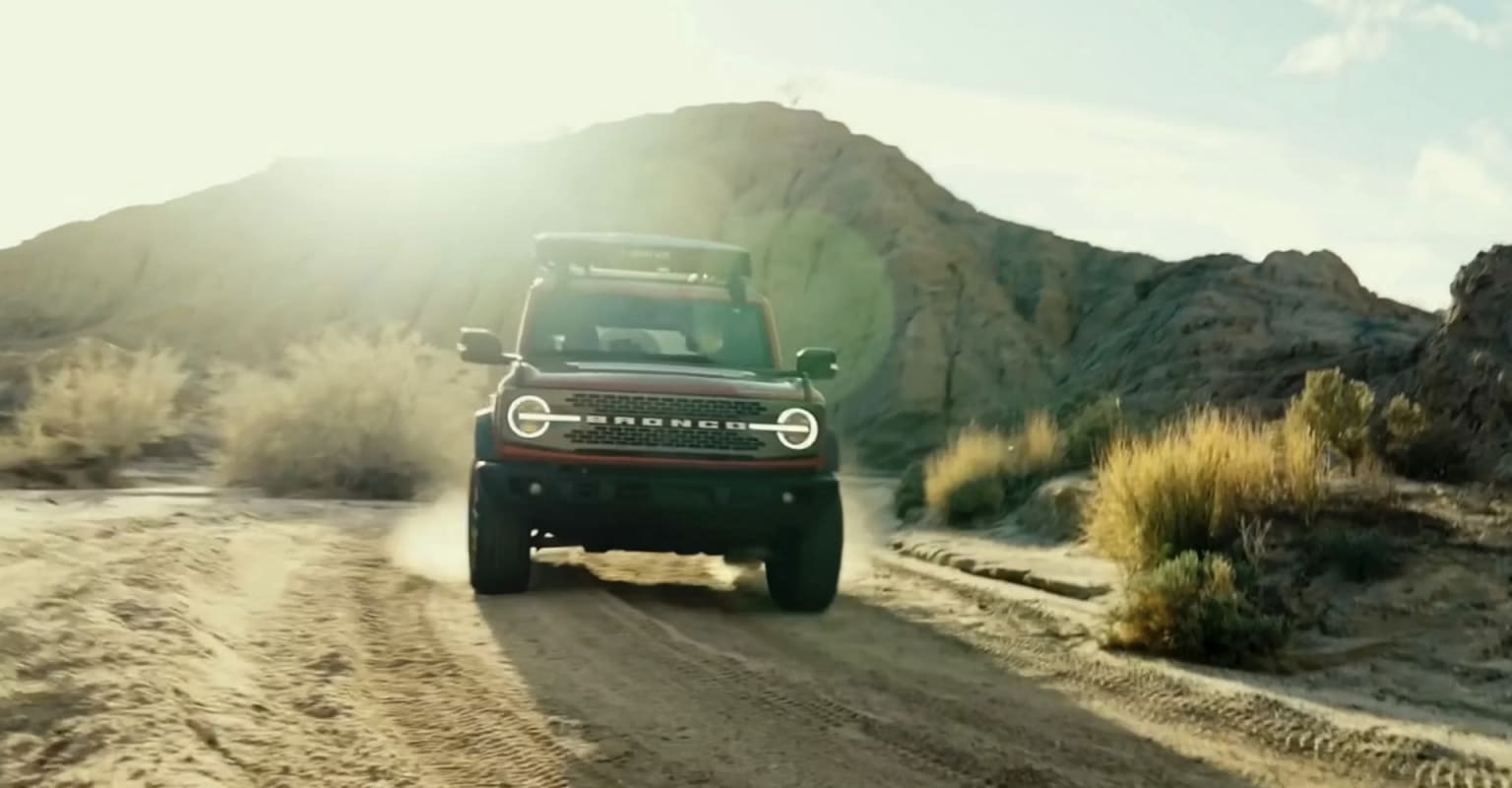 Off-road vehicle on dusty desert road with mountains and sky