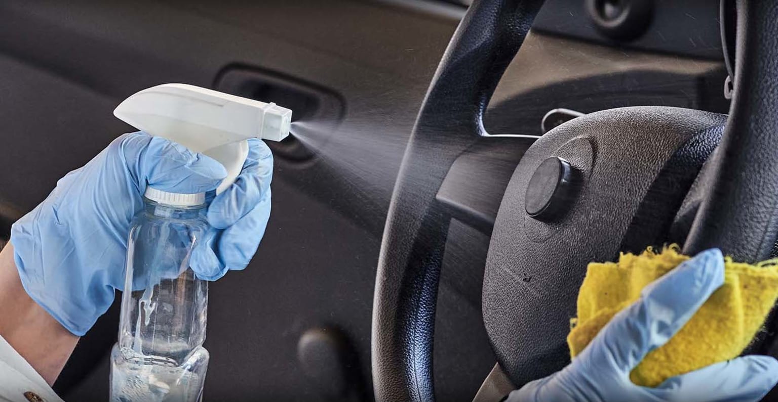 a person in blue gloves is cleaning a car with a spray bottle and a sponge on the dash of the car