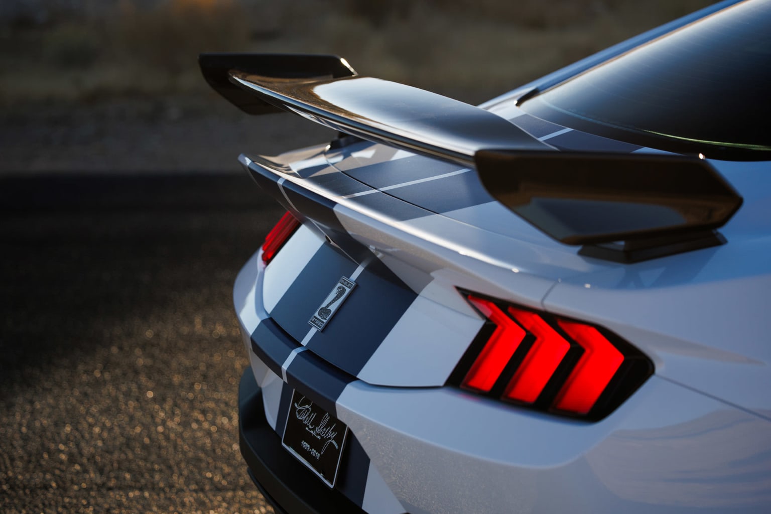A sleek, white sports car with a prominent rear spoiler and distinctive taillights stands in a dimly lit environment, casting a dramatic shadow on the ground.