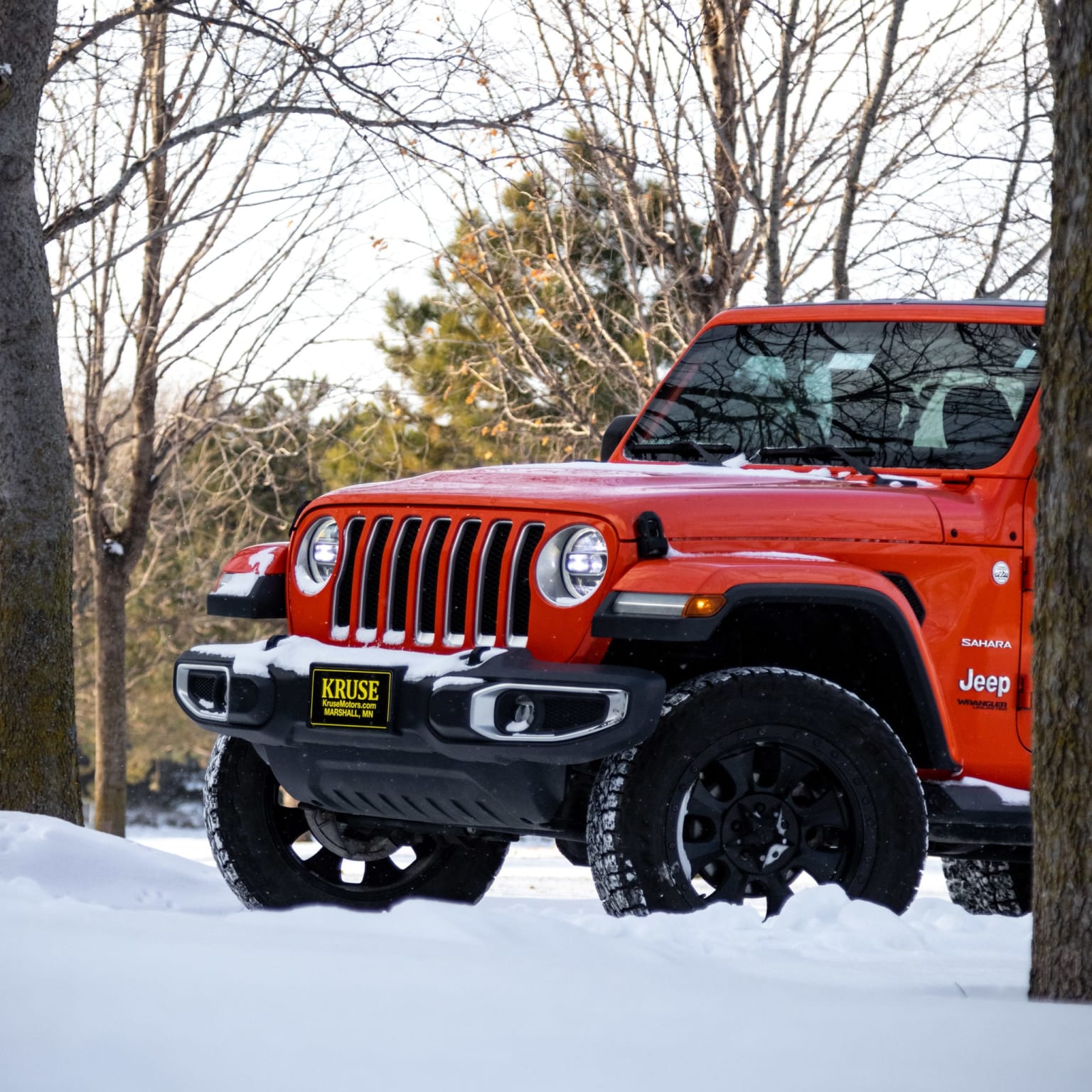 a red jeep is parked in the snow near some trees and a sign that says jeep on the side of the jeep