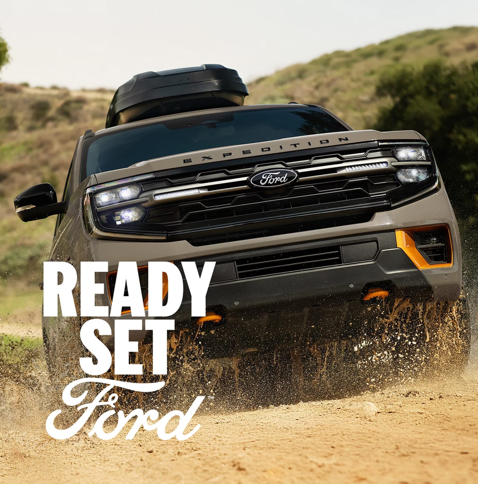 A rugged truck with text prominently displayed, driving through a dusty, hilly terrain in the background.