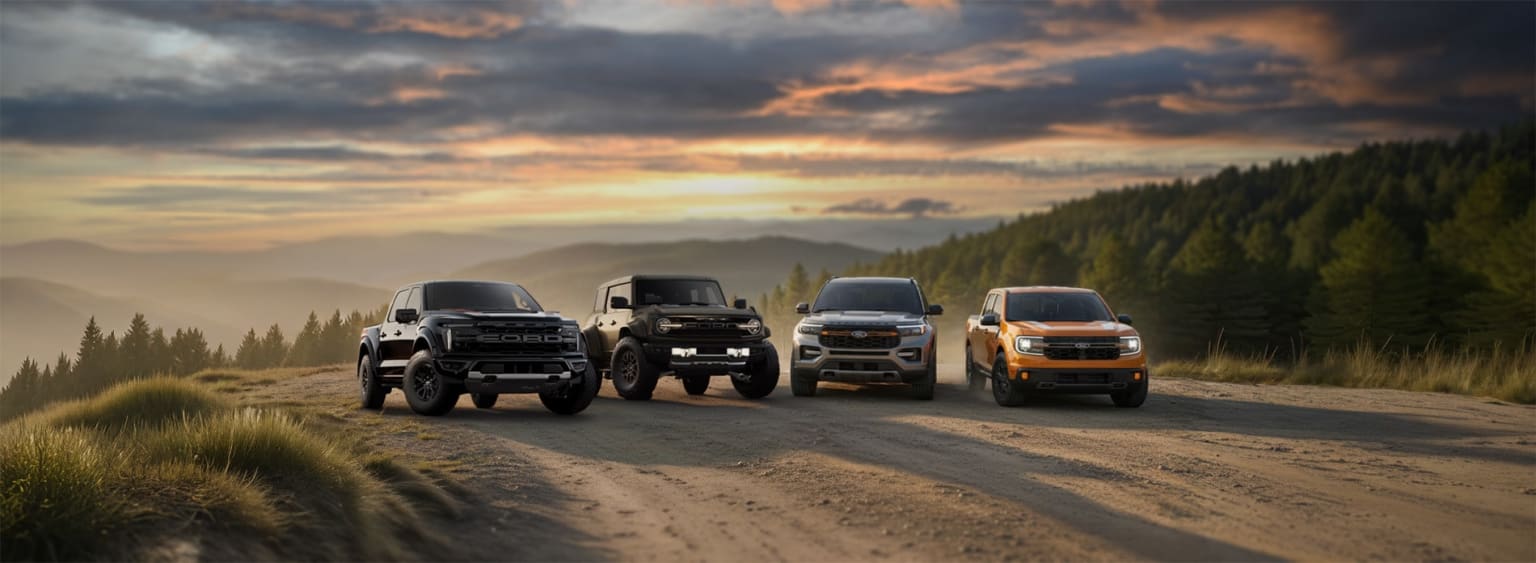 A group of rugged off-road vehicles traversing a dirt road against a backdrop of a dramatic sunset sky and mountainous terrain.