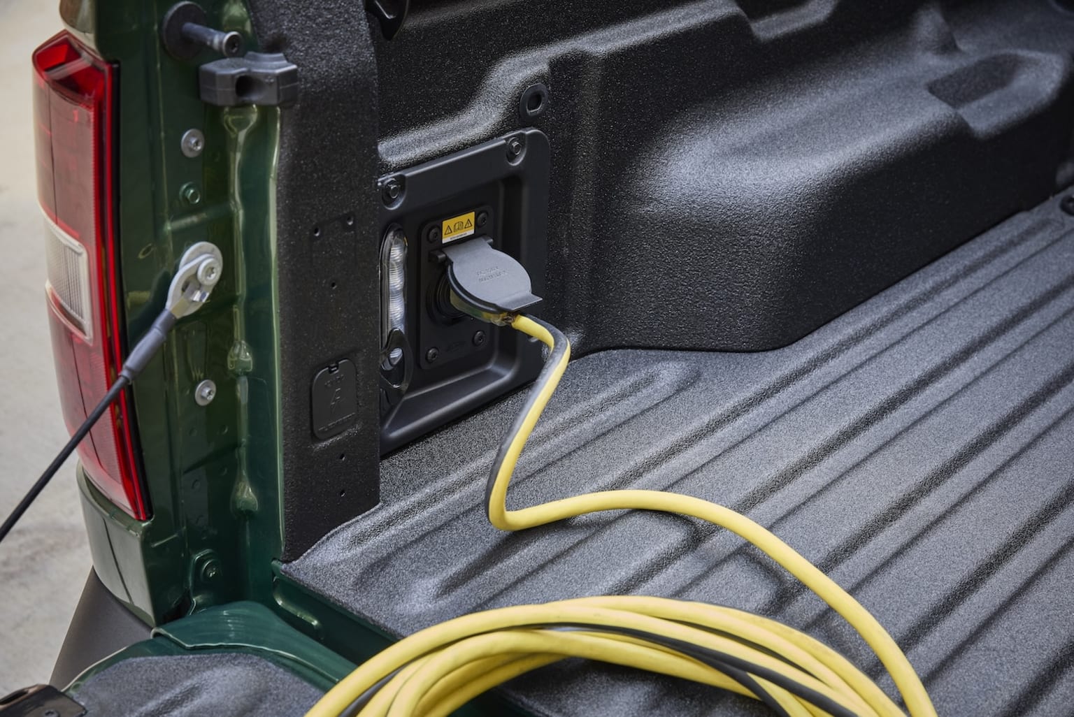 Interior of a truck bed with a green toolbox and a yellow electrical cord plugged into a power source.