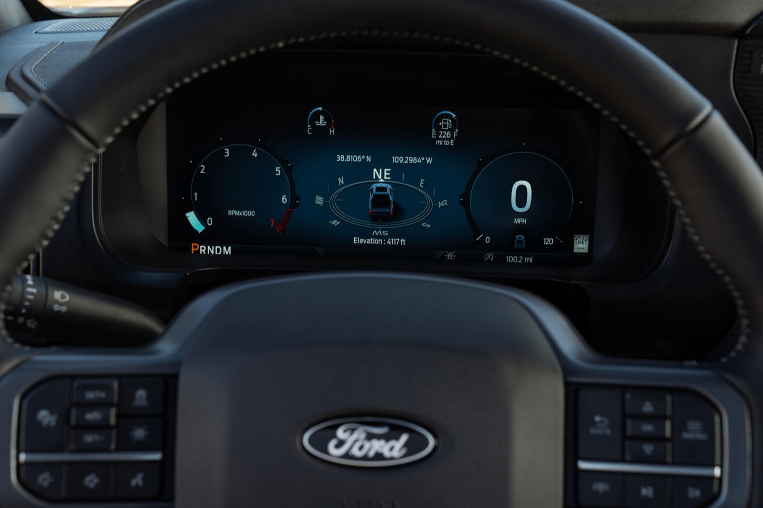 The image shows the dashboard and steering wheel of a vehicle, with various digital displays and controls visible in the foreground.