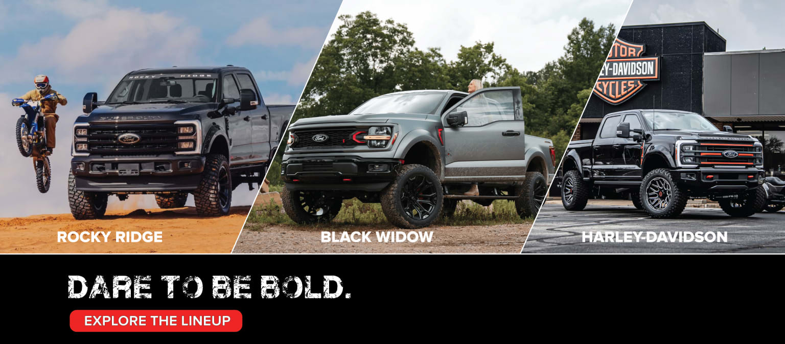Customized pickup trucks displayed outdoors in a lush green setting with a cloudy sky. The trucks are part of a promotional lineup encouraging viewers to "Dare to be bold" and "Explore the lineup."