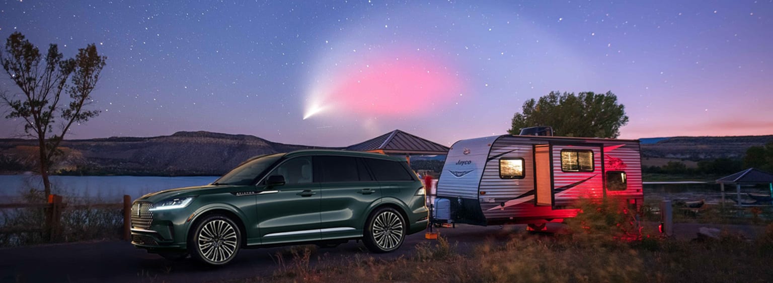 A large green SUV parked next to a colorful camper trailer under a starry night sky, with a bright comet-like object illuminating the scene.