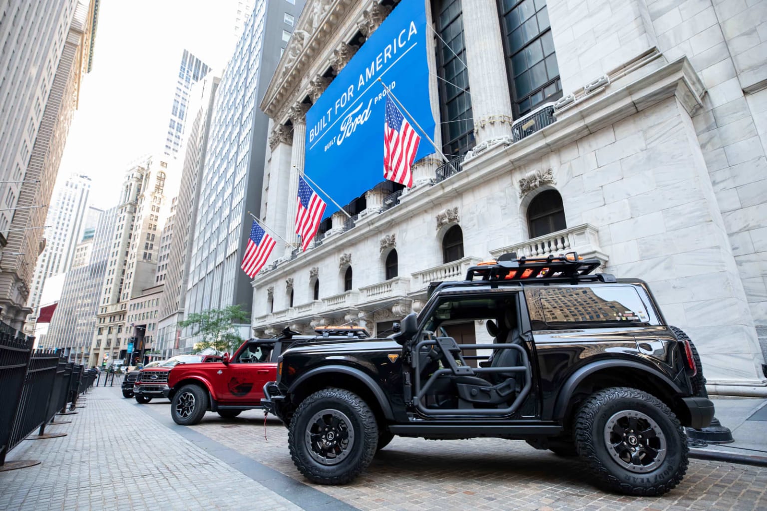 a jeep is parked in front of a wall street building with american flags hanging from the side of the building