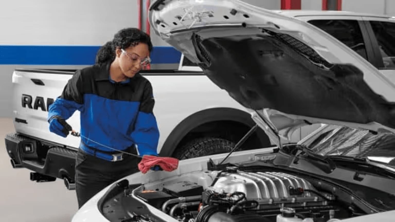 A mechanic in a blue and black uniform is inspecting the engine of a vehicle in a garage setting.