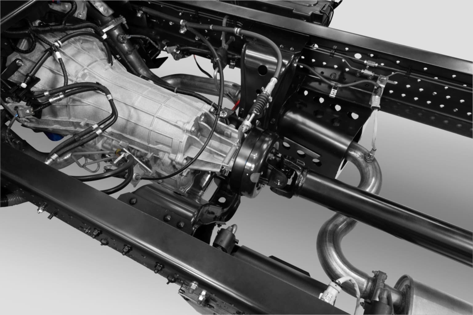 Close-up of intricate mechanical components and wiring of a complex machine or engine with various metal parts, tubes, and cables visible in the foreground against a dark background.