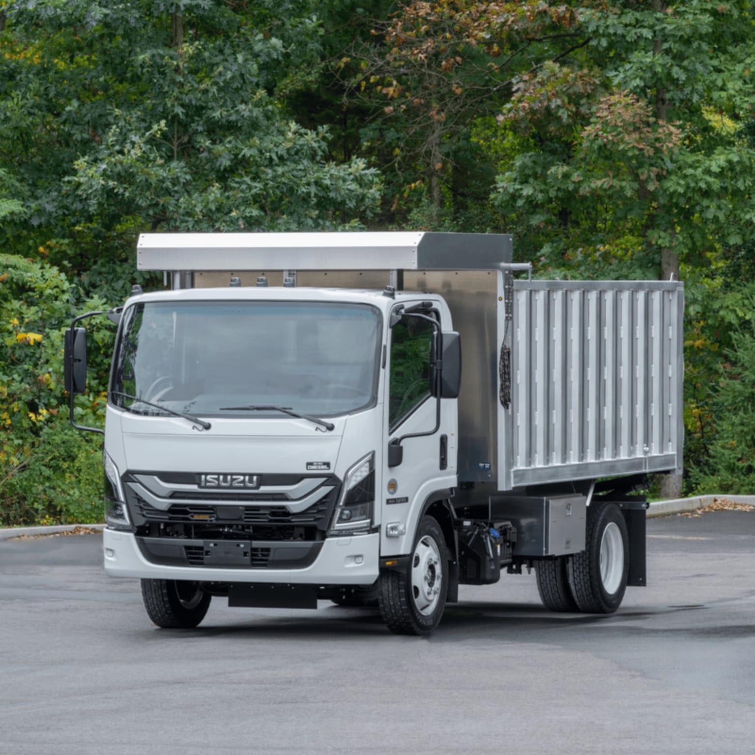 A white dump truck is parked on a paved surface against a backdrop of lush green trees.